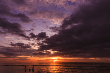 Fototapeta premium Silhouette of family members join hands to play in the sea at sunset with sun shines on the surface of the sea