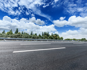 asphalt road and green forest under the blue sky