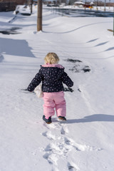 Fototapeta na wymiar Toddler in snowsuit making tracks in the fresh snow