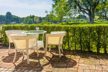 Vintage outdoor white wicker furniture in garden. There are a table and three chairs.