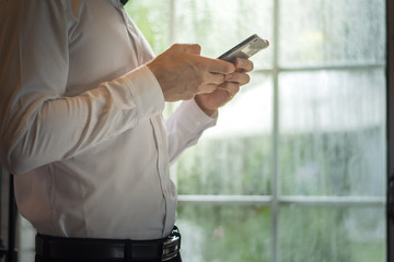 Businessman using a smartphone while standing at a window on a rainy day