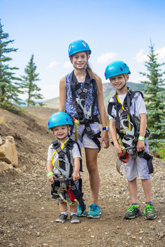 Smiling group of cute kids ready to go on a zip line adventure in the mountains while on a summer vacation together

