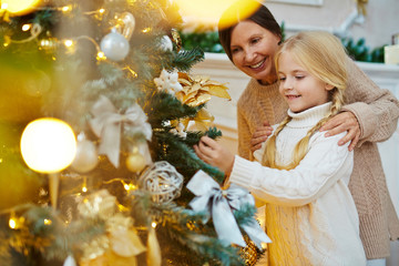 Happy grandmother helping her granddaughter hang xmas toys on firtree