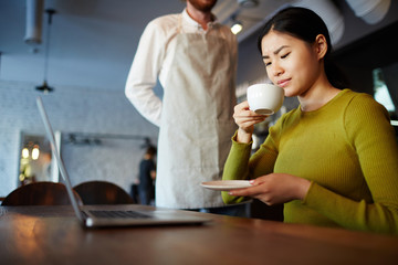 Displeased female with cup of drink smelling it and expressing dislike