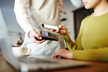 Visitor of cafe transfering money through modern mobile payment app in her smartphone