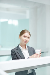 Waist-up portrait of attractive young manager in formalwear posing for photography while enjoying fragrant coffee at spacious office lobby