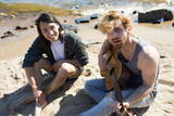 Young man playing guitar and singing on seashore with his friend on background