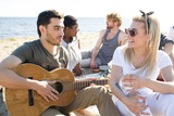 Young man with guitar listening to his girlfriend with drink during talk
