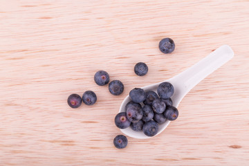 Organic blueberries scooped in spoon on wooden surface