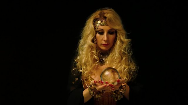Beautiful blond astrologer woman looking through crystal ball. Fortune telling.