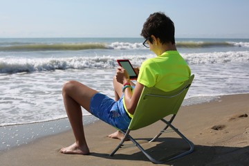 young boy reads an ebook at the seaside