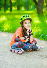 Happy girl in a protective helmet and protective pads for roller skating sitting on the road