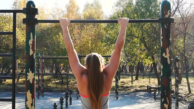 Powerlifting girl pulls up on the crossbar at sports ground