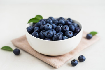 Juicy and fresh blueberries with green leaves on white bowl. Healthy eating