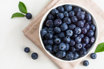 Juicy and fresh blueberries with green leaves on white bowl. Healthy eating