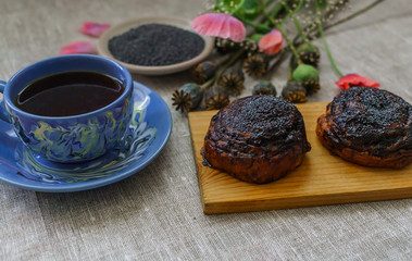 Sweet bun with flax seed and poppy and cup of tea on table.