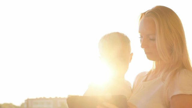Mother and son using tablet on vacation at sunset.