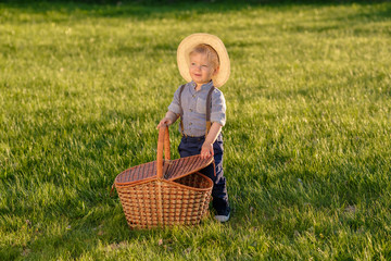 Toddler child outdoors. One year old baby boy wearing straw hat with picnic basket