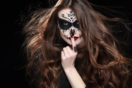 Beautiful woman with Halloween sugar skull makeup showing silence gesture. Shh! Close up studio portrait. 
