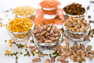 A beautifully arranged assortment of legumes and pulses in glass bowls, featuring red kidney beans (Rajma), chana dal, and white chickpeas (Kabuli Chana). These protein-rich ingredients are widely use