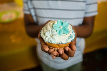 Mid section of boy holding decorated cupcake during birthday