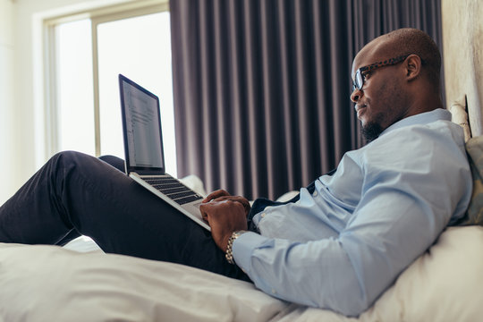 Businessman working on laptop computer lying on bed