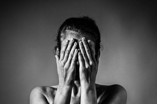 Concept of fear, shame, domestic violence. Woman covers her face her hands on light  scratched background. Black and white image.