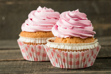 Closeup of cupcakes with vanilla, berries, pink and white cream, chocolate and sprinkles on wooden background. Selective focus. Sweet dessert tasty food concept muffin.