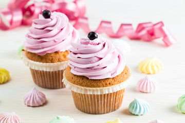 Closeup of cupcakes with vanilla, berries, pink and white cream, chocolate and sprinkles on wooden background. Selective focus. Sweet dessert tasty food concept muffin.