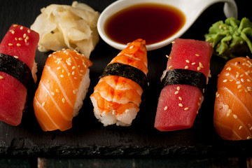 Sashimi and sushi rolls on a stone slatter. Sushi set with salmon, prawns, soy souce, wasabi and ginger. Traditional Japanese cuisine.