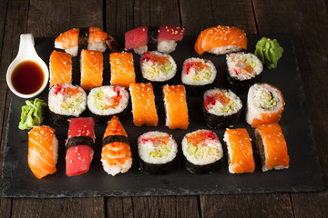 Sashimi and sushi rolls on a stone slatter. Sushi set with salmon, prawns, soy souce, wasabi and ginger. Traditional Japanese cuisine.