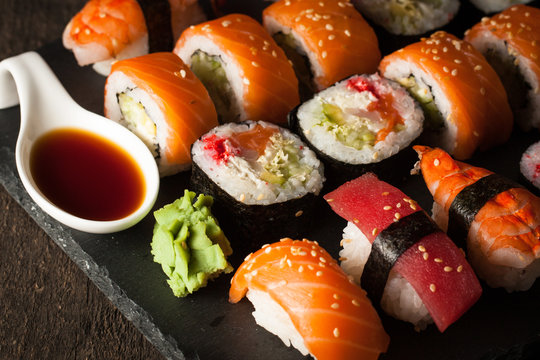 Sashimi and sushi rolls on a stone slatter. Sushi set with salmon, prawns, soy souce, wasabi and ginger. Traditional Japanese cuisine.