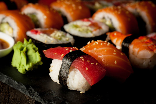 Sashimi and sushi rolls on a stone slatter. Sushi set with salmon, prawns, soy souce, wasabi and ginger. Traditional Japanese cuisine.