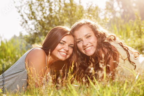 Two Young Women Lying Down On Green Grass Smiling Happy