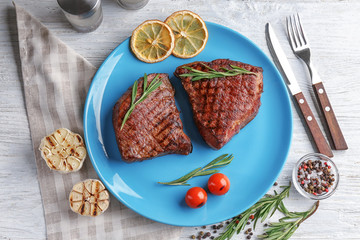 Plate with delicious grilled steaks on wooden table