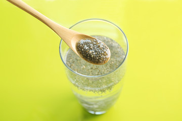 Spoon and glass of water with chia seeds on color background