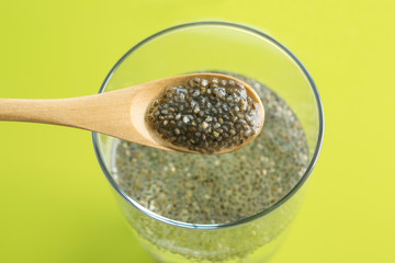 Spoon and glass of water with chia seeds on color background