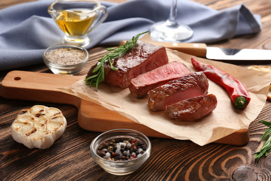 Board with yummy grilled steak on wooden table