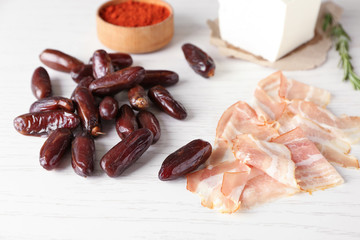 Ripe dates and raw bacon strips on light background