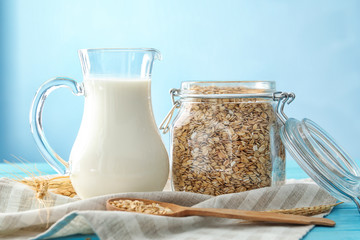 Jar with oatmeal flakes and pitcher of milk on light background