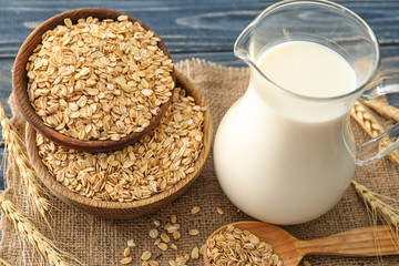 Wooden bowls with oatmeal flakes and pitcher of milk on sackcloth fabric