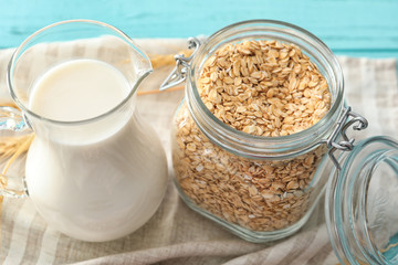 Jar with oatmeal flakes and pitcher of milk on fabric
