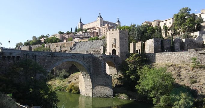 4k video. Shot from green water river Tagus, Tajo in Spanish, of Alcantara arch bridge and door,  landmark and monument from ancient Roman age, in Toledo city, Spain, Europe
