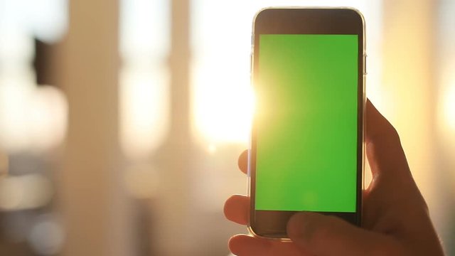 close up man hand holding black telephone smart phone green screen chroma key golden sun light sunshine background sunny day internet searching application store notification weblink online video call