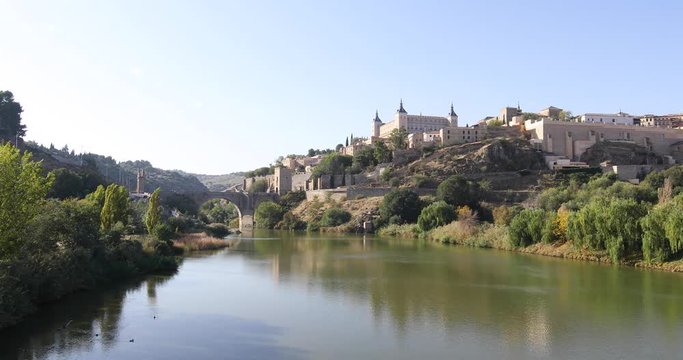 4k video. Scenery of Toledo city, in Spain, Europe. Green water river Tagus, Alcantara arch bridge, landmark and monument from ancient Roman age, and alcazar building
