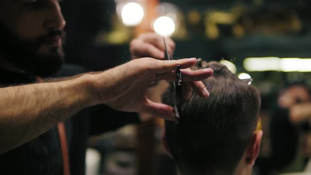 Closeup view of the barber's hands performing a haircut with scissors and combing the client. Slowmotion shot
