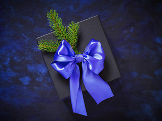 Christmas gift Stylish black on blue-black background. Decorated with a bow of blue ribbon and fir tree branches.