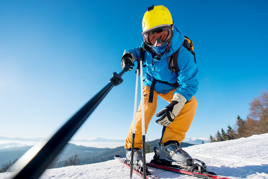Low angle shot of a professional skier taking a selfie using monopod posing on top of a slope in the mountains, copyspace ski resort recreation travelling tourism vacation extreme adrenaline