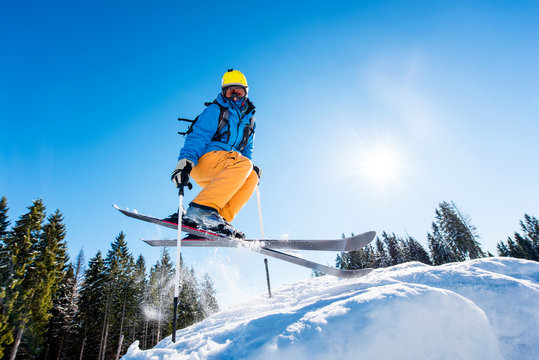 Low angle shot of a skier in colorful gear jumping in the air while skiing on a slope copyspace sunlight extreme adrenaline enjoyment recreation activity concept
