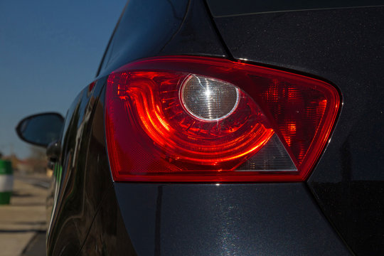 Detalle de Faro rojo trasero de coche de color negro metalizado, en forma de ojo,  con reflejo del sol en la pupila